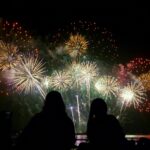 People watching beautiful fireworks together by the sea at night.