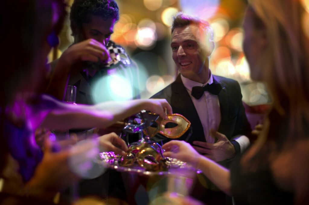 Man in tuxedo handing over eye masks on a costume party