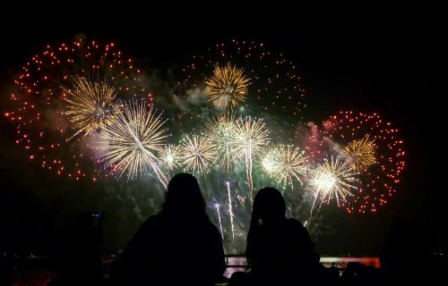 People watching beautiful fireworks together by the sea at night.